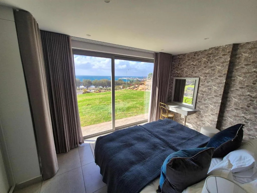 Modern bedroom with ocean view through large sliding glass doors and green lawn