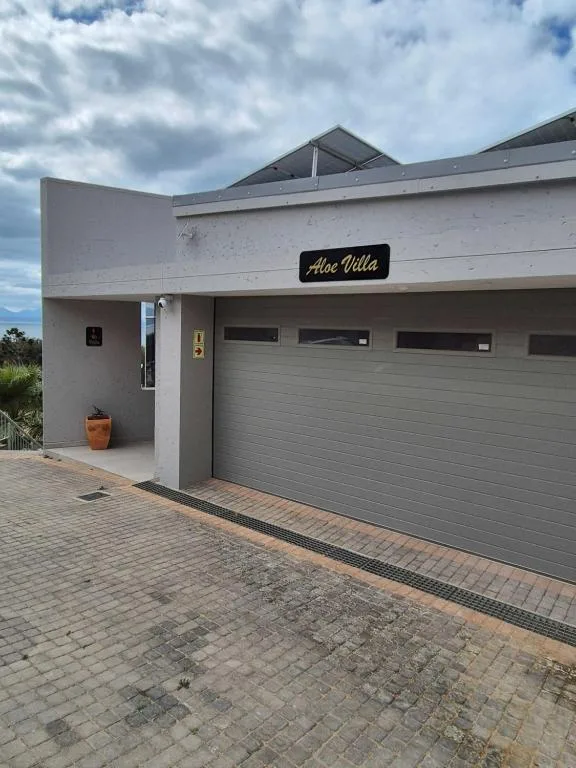Modern white villa entrance with gray garage doors and paved driveway