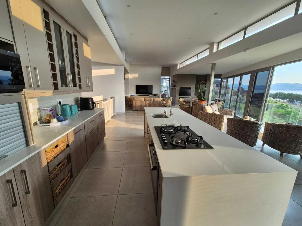 Modern kitchen with white island, gas cooktop, and garden views through large windows