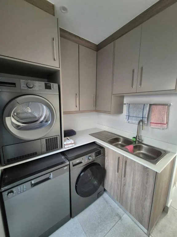 Modern kitchen with laundry appliances, sink, and white cabinetry