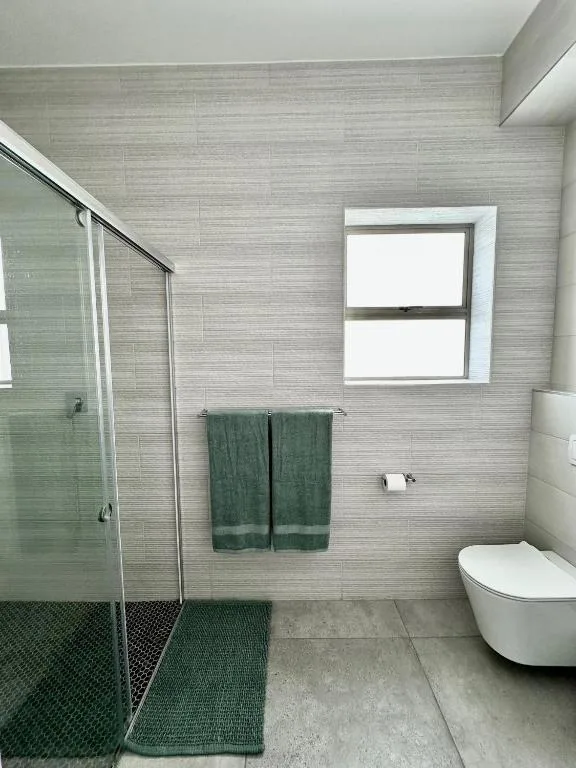 Modern bathroom with walk-in shower, toilet, and green towels