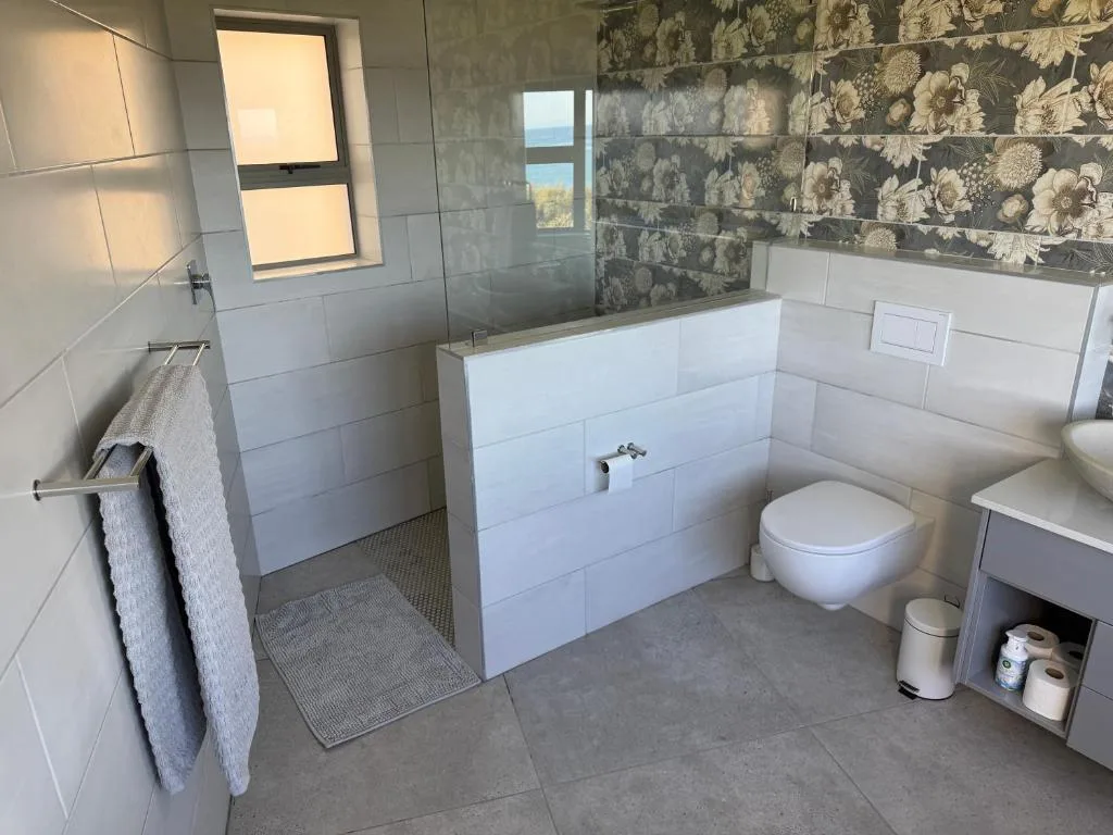 Modern bathroom with walk-in shower, toilet, vanity, and decorative tile accent wall