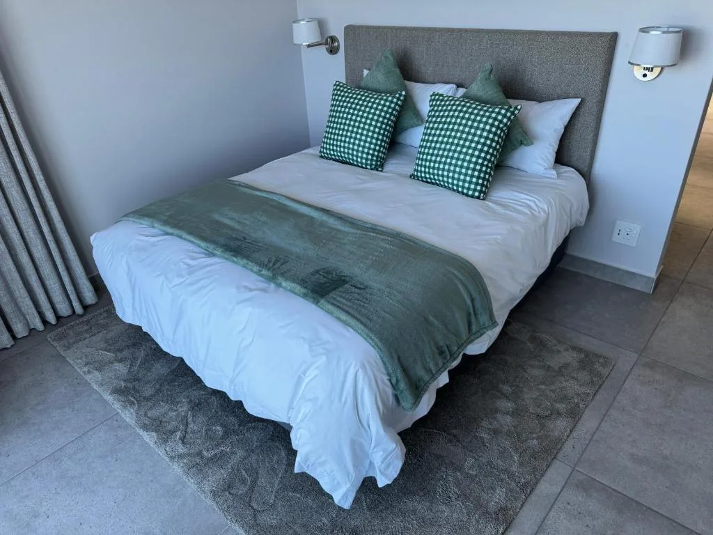 Neatly made bed with green checkered pillows and gray upholstered headboard