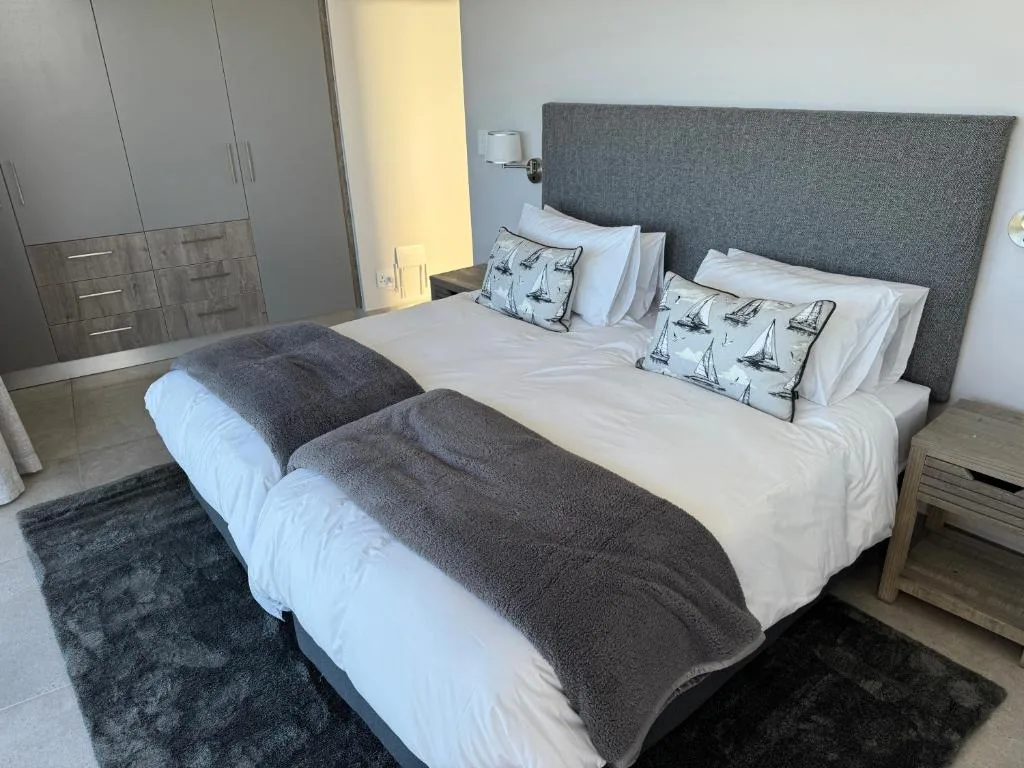 Modern bedroom with twin beds, gray headboard, white linens, and sailboat cushions