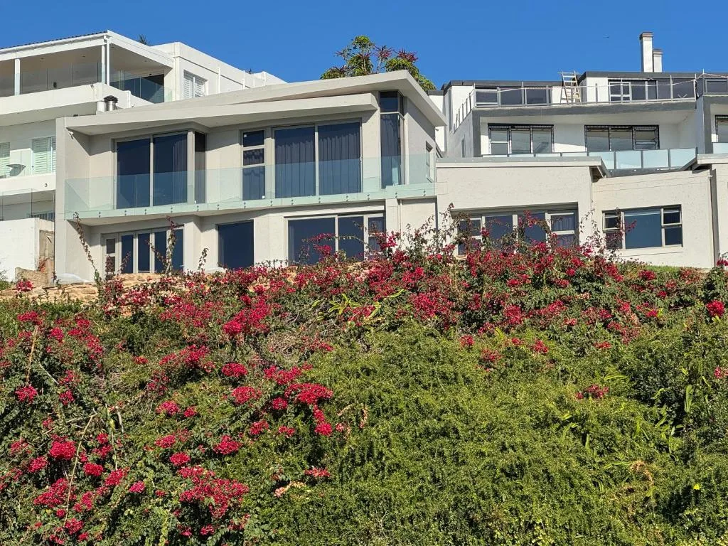 Modern white villa with large windows surrounded by blooming red bougainvillea flowers
