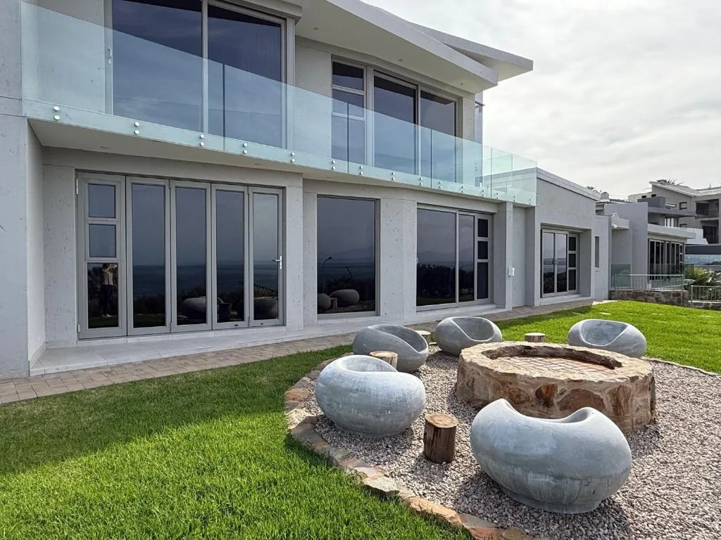 Modern two-story white villa with glass balcony and large sliding doors overlooking manicured lawn