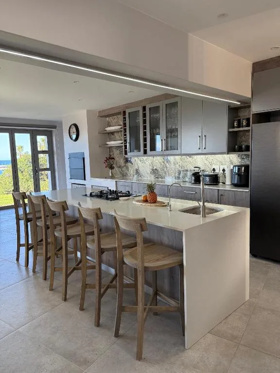 Modern kitchen with white island, marble backsplash, and ocean view through doors