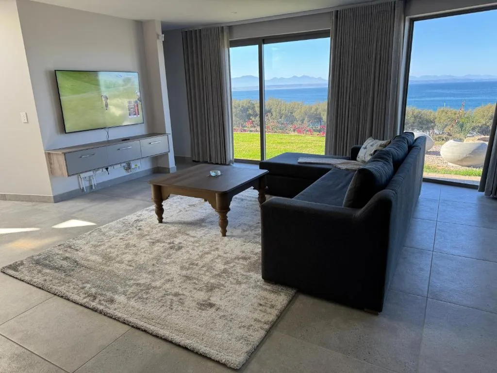 Modern living room with black sofa, TV, and ocean views through large windows