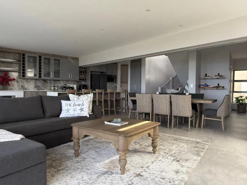 Open-plan lounge with dark sofa, wooden coffee table, and dining area beyond