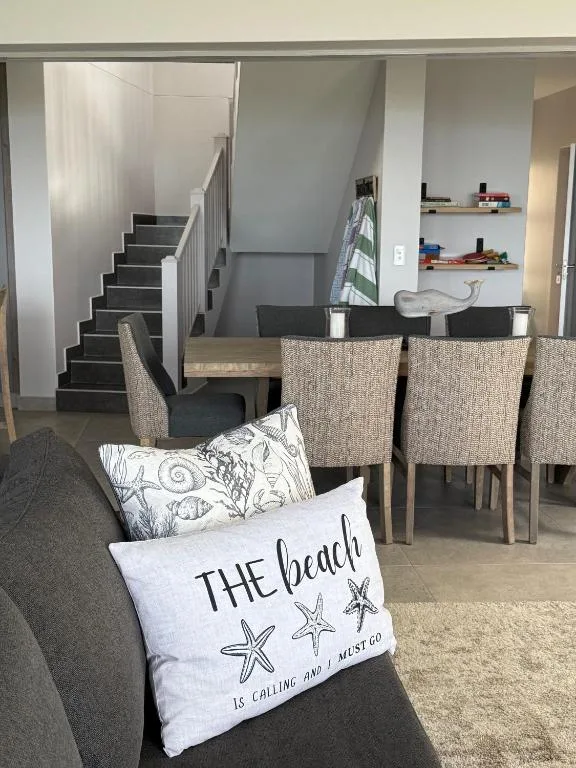 Open-plan lounge with grey sofa, beach-themed cushion, dining area visible beyond