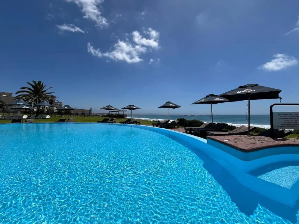 Expansive swimming pool overlooking ocean with umbrellas and beach beyond