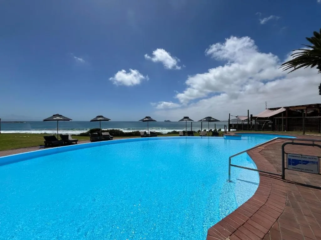 Large swimming pool overlooking ocean beach with umbrellas and loungers