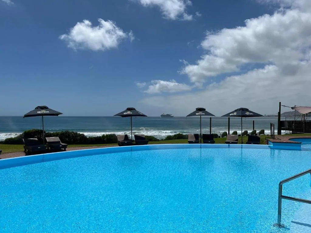 Oceanfront swimming pool with umbrellas overlooking turquoise sea