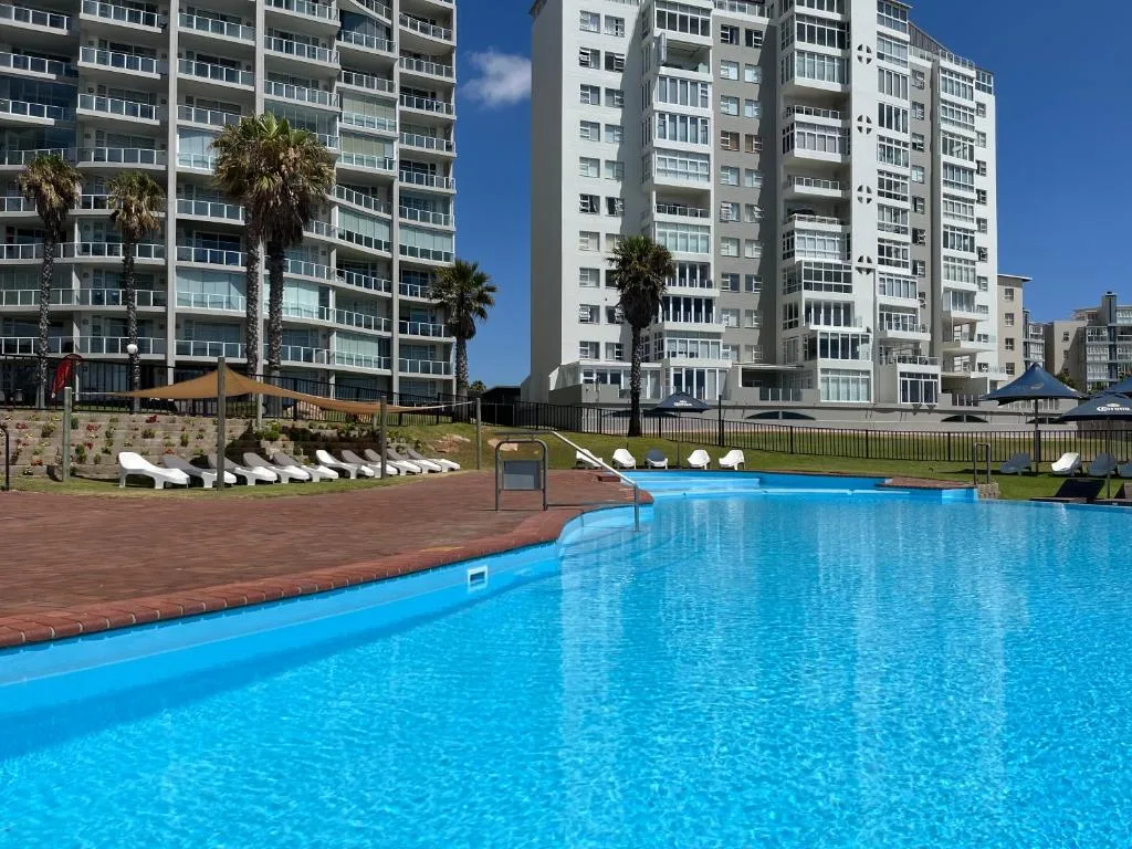 Large bright blue swimming pool with loungers and apartment buildings backdrop