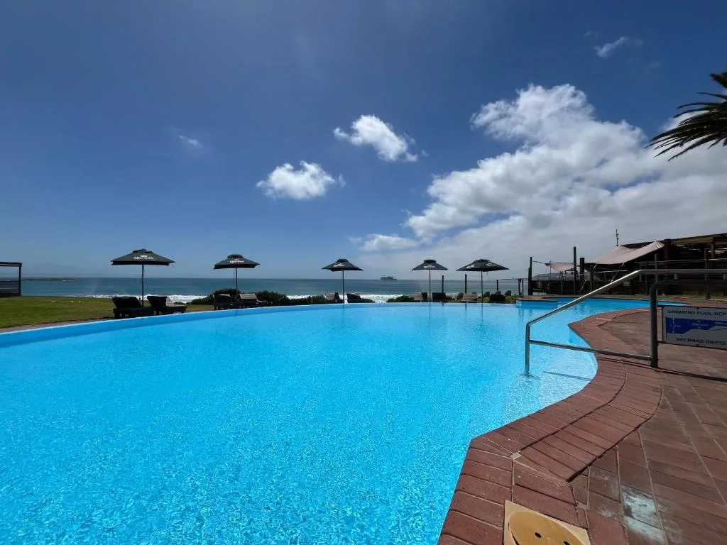 Large curved swimming pool with ocean view, umbrellas and loungers beyond