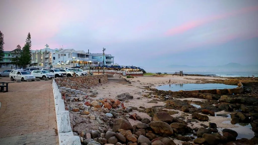 Beachfront building with parking and rocky shoreline at dusk
