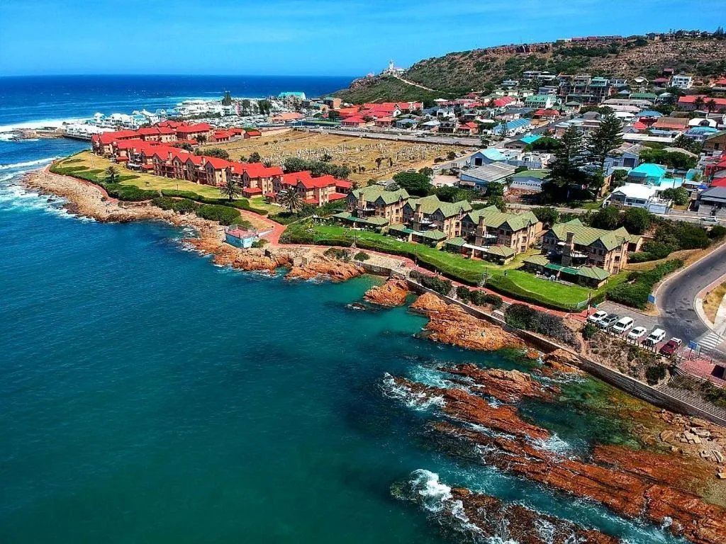 Aerial view of coastal town with turquoise ocean, red-roofed buildings, and rocky coastline