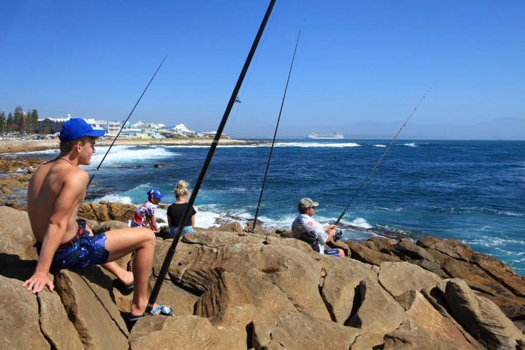 Scenic ocean view from rocky coastline with fishing enthusiasts and distant coastal town