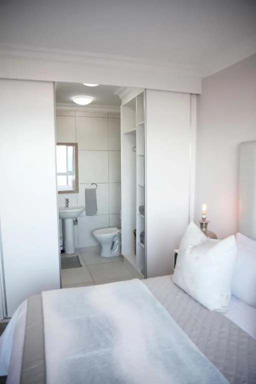 Bright bedroom with white bedding and en-suite bathroom visible through open glass doors