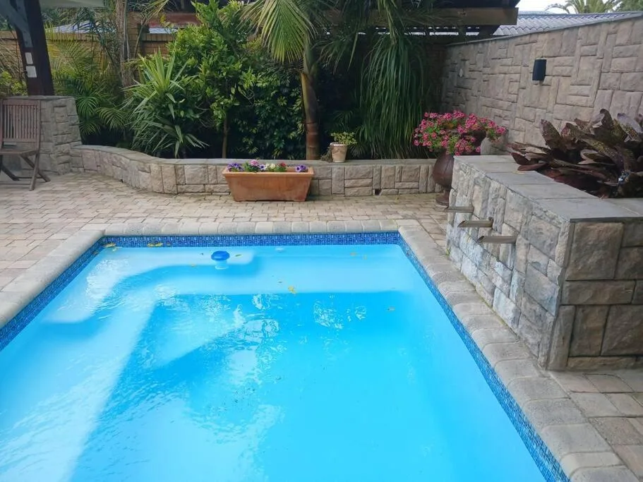 Bright blue swimming pool with surrounding paved deck and landscaped gardens