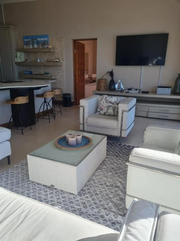 Modern lounge with cream armchairs, TV, and open-plan kitchen area