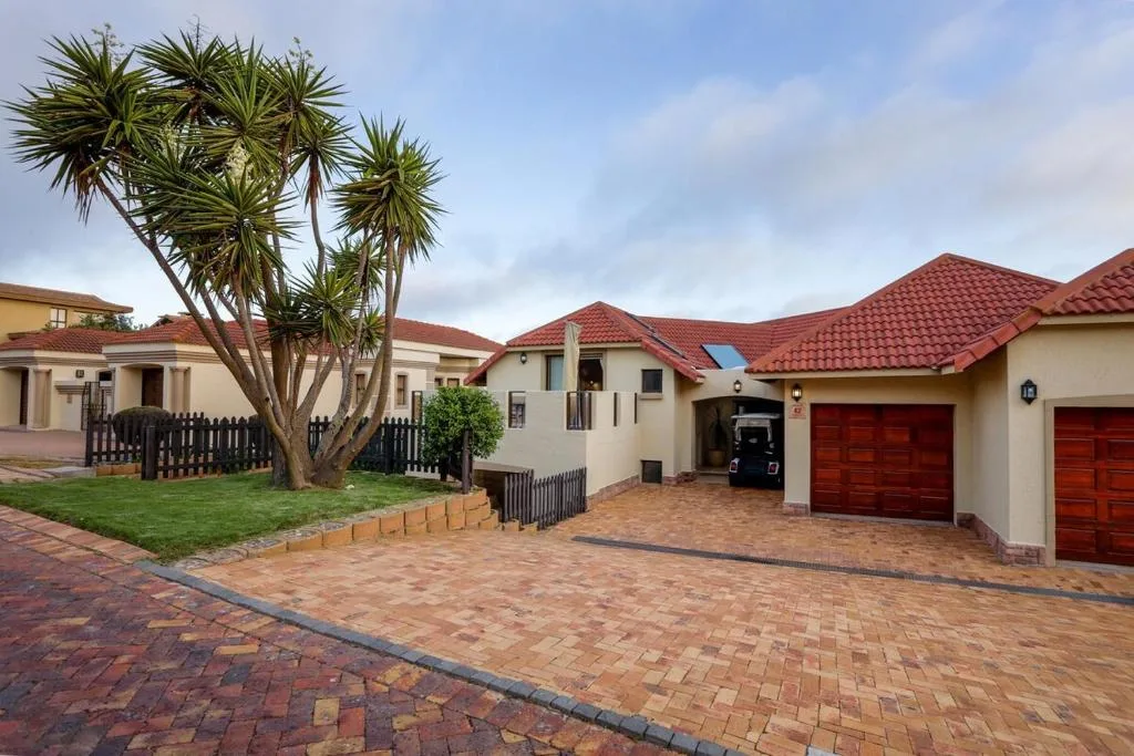 Modern villa with red tile roof, brick driveway, and tropical palm tree