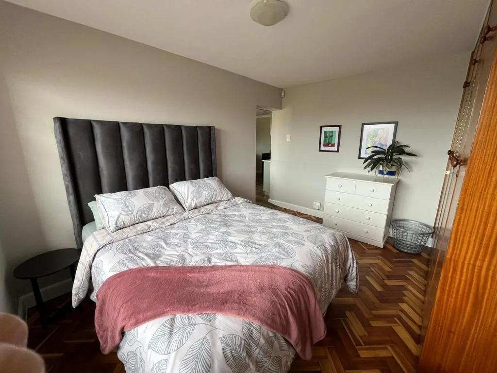 Spacious bedroom with queen bed, dark headboard, white dresser, and wooden floors