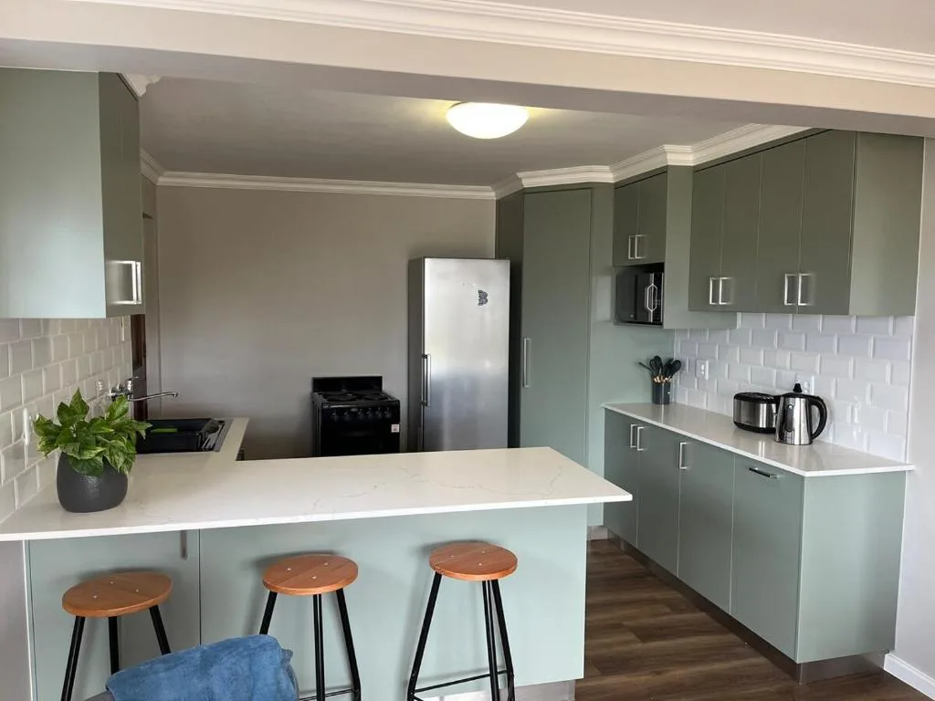 Modern kitchen with sage green cabinetry, white counters, and bar seating