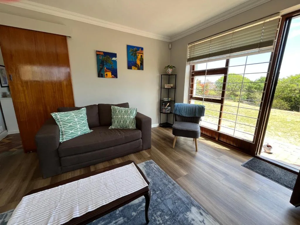 Bright lounge with dark sofa, colorful pillows, and garden views through large windows