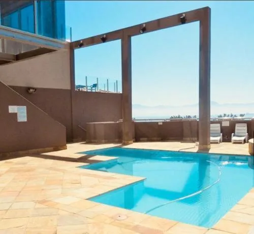 Bright blue swimming pool on sunny terrace with ocean view beyond