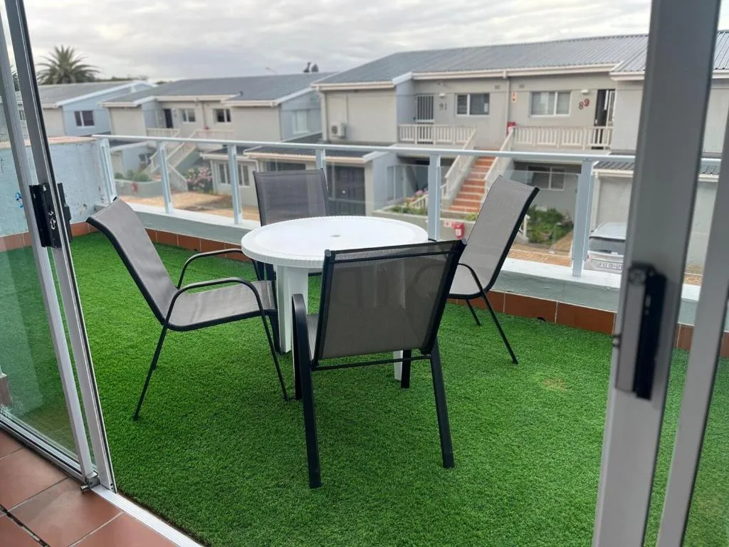 Outdoor patio with round table, chairs, and artificial grass overlooking complex