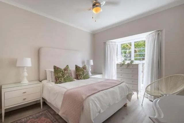 Bright bedroom with upholstered headboard, white bedding, and garden views through windows