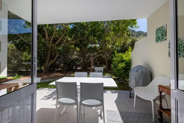 Shaded patio with white chairs overlooking mature trees and garden
