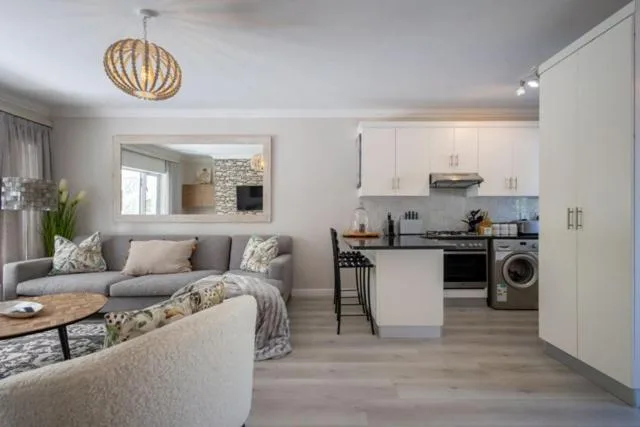 Open-plan lounge with gray sofa, woven pendant light, kitchen visible beyond