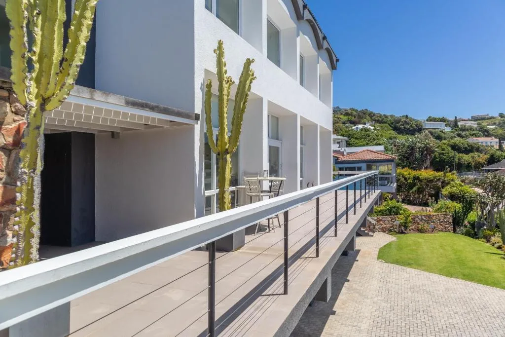 Modern white building facade with deck railing and manicured garden