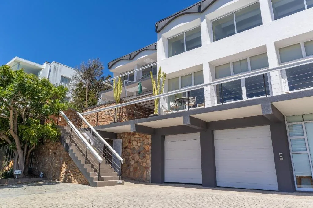 Modern white multi-story building with garage, stairs, and deck railings