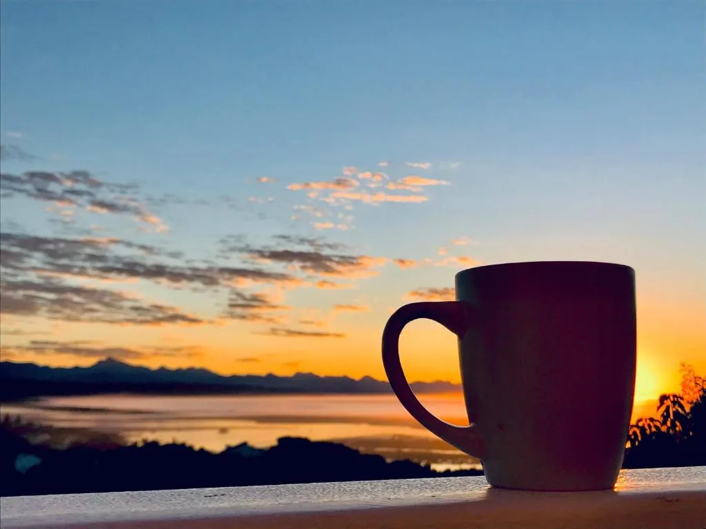 Steaming mug silhouetted against golden sunset over lagoon and mountains