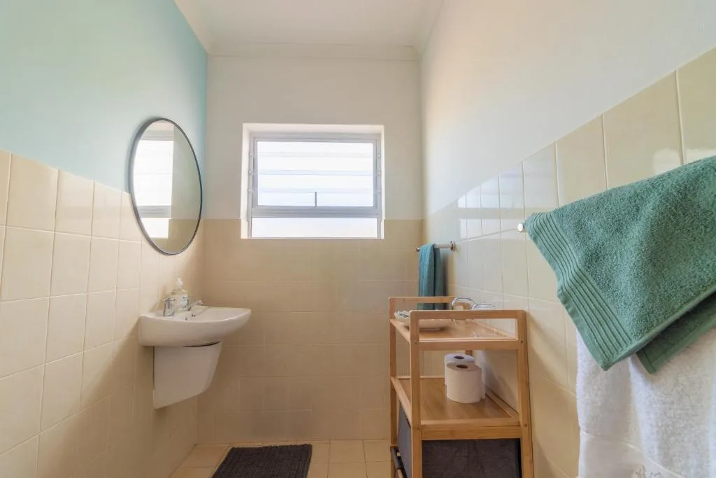 Bright bathroom with cream tiles, round mirror, and window overlooking garden