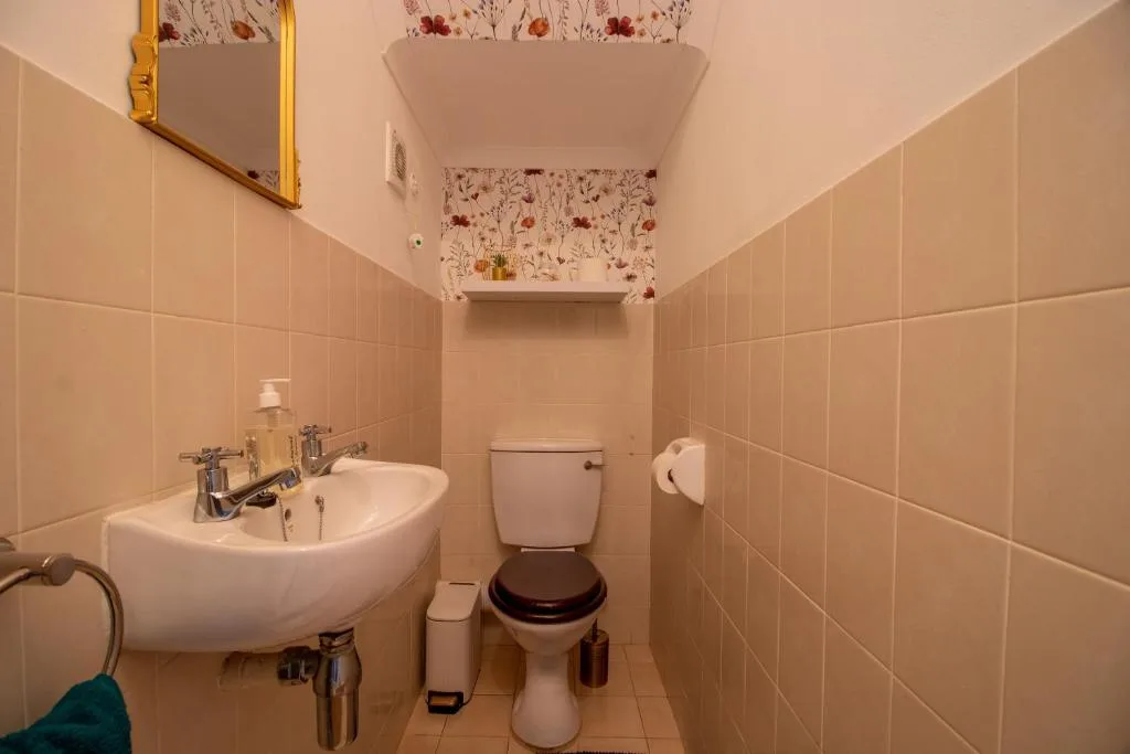 Compact bathroom with curved sink, toilet, and floral wallpaper accent