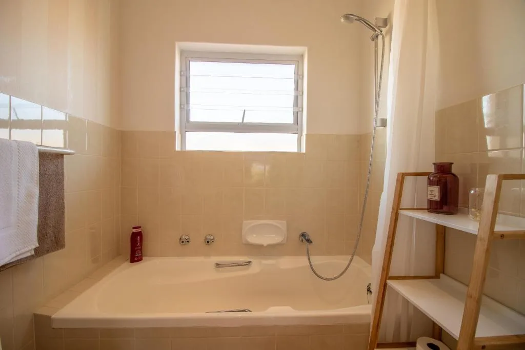 Cream-tiled bathroom with bathtub, shower head, and wooden shelving unit