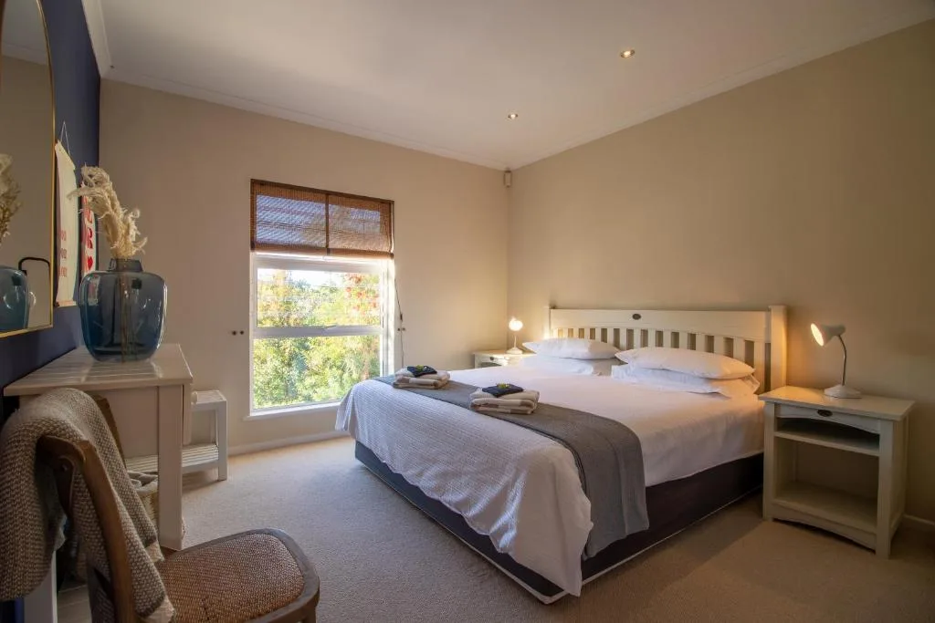 Bright bedroom with double bed, white linens, wooden headboard, and garden views