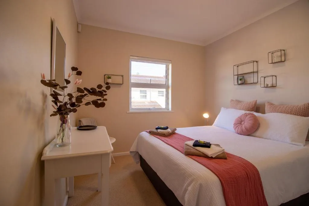 Bright bedroom with queen bed, pink cushions, and flowering plant on bedside table