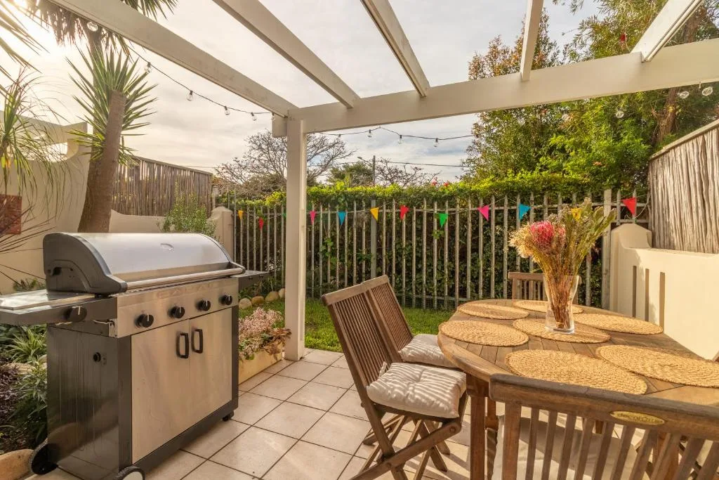 Covered patio with braai, dining table, and colorful garden fence views