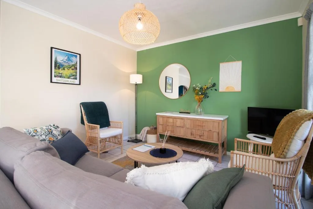 Modern lounge with grey sofa, green accent wall, wicker chairs, and TV