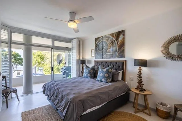 Modern bedroom with queen bed, ceiling fan, and glass doors opening to garden view