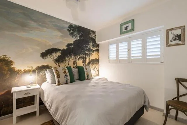 Bedroom with large landscape mural headboard and natural light from shuttered windows