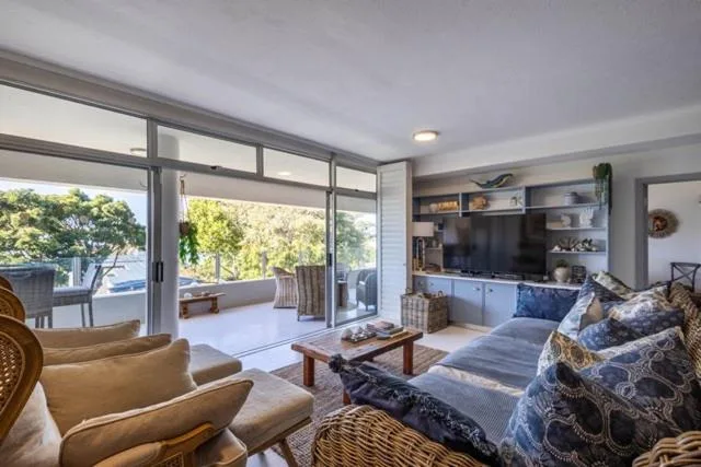 Modern lounge with sofa, armchair, TV unit, and glass doors to deck