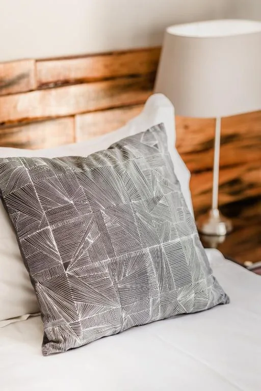 Decorative patterned pillow on bed with wooden headboard and lamp