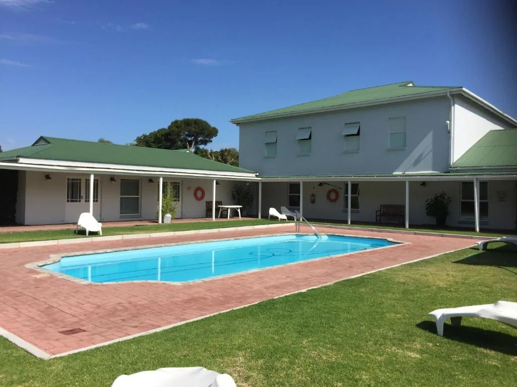 Rectangular swimming pool with brick surround and white loungers on manicured lawn