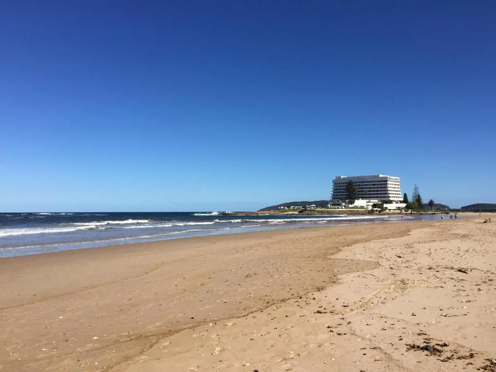 Sandy beach with ocean waves and beachfront hotel building under clear blue sky